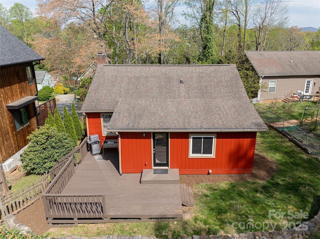 back of house featuring roof with shingles, fence, a wooden deck, a chimney, and board and batten siding