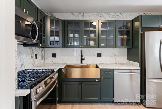 kitchen featuring glass insert cabinets, appliances with stainless steel finishes, decorative backsplash, and a sink