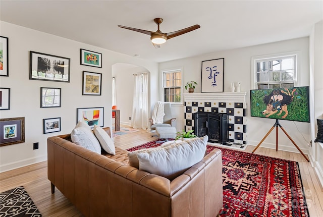 living area featuring ceiling fan, hardwood / wood-style floors, arched walkways, and a fireplace with flush hearth