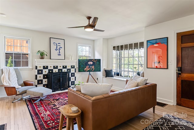 living room featuring wood finished floors, visible vents, a fireplace, a ceiling fan, and baseboards