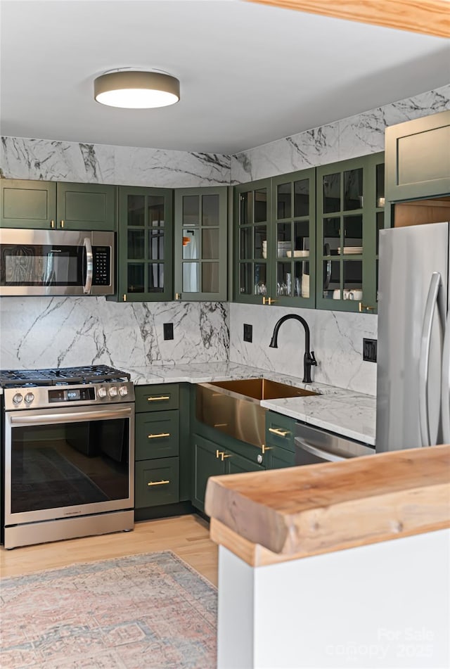 kitchen with green cabinets, a sink, wood counters, backsplash, and appliances with stainless steel finishes