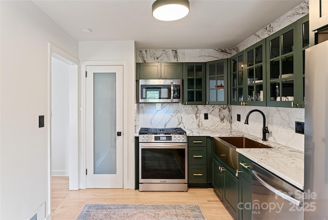 kitchen with light wood-style flooring, a sink, green cabinets, backsplash, and appliances with stainless steel finishes