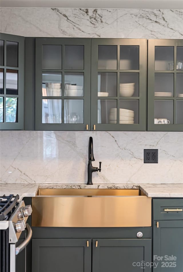 interior space featuring glass insert cabinets, a sink, stainless steel range with gas stovetop, light countertops, and decorative backsplash