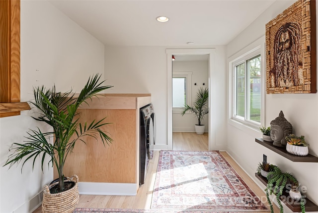 hall featuring light wood-style flooring, baseboards, washer / clothes dryer, and recessed lighting