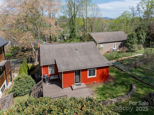 rear view of property featuring roof with shingles, fence, a wooden deck, a chimney, and a lawn