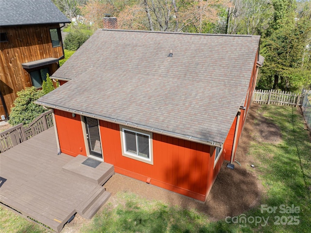 back of property with a chimney, a deck, roof with shingles, and fence