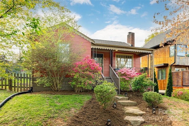 view of front of home featuring covered porch, roof with shingles, fence, and a chimney