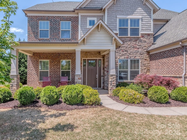 craftsman house featuring stone siding, a shingled roof, a front lawn, and covered porch