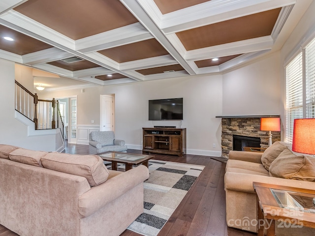 living room featuring dark wood-style floors, beam ceiling, coffered ceiling, stairs, and a stone fireplace