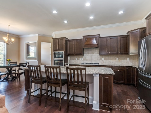 kitchen with an inviting chandelier, custom exhaust hood, dark brown cabinets, and stainless steel appliances