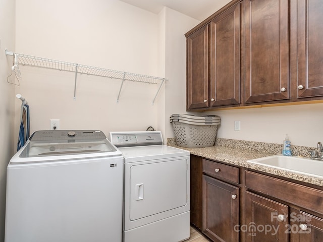 clothes washing area featuring washing machine and dryer, cabinet space, and a sink