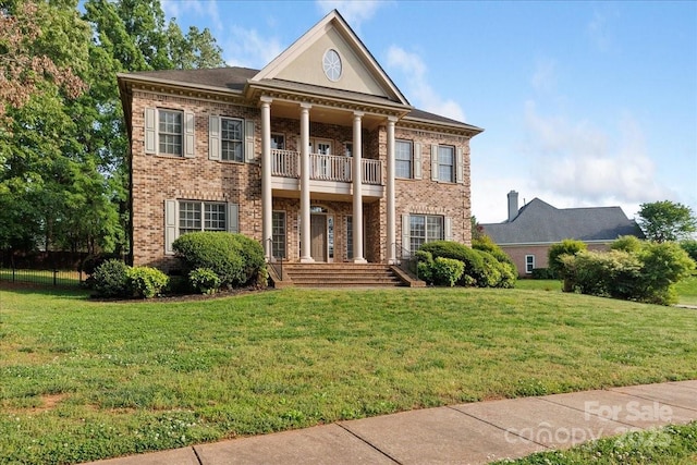 neoclassical / greek revival house featuring brick siding, a balcony, and a front yard