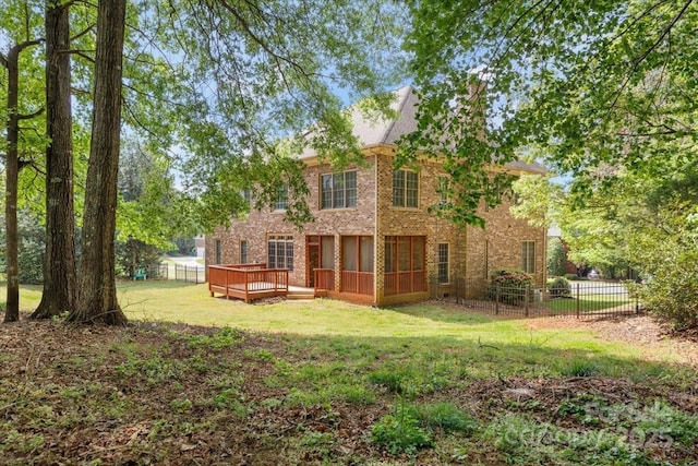 rear view of house featuring a sunroom, a wooden deck, fence private yard, a lawn, and brick siding