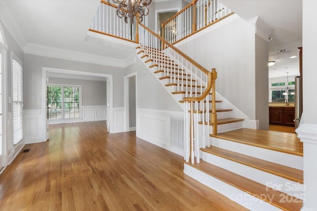 staircase featuring ornamental molding, a notable chandelier, a wainscoted wall, and wood finished floors