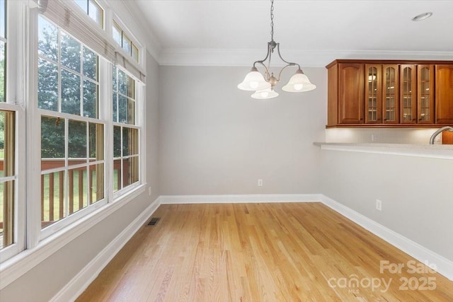 unfurnished dining area featuring light wood finished floors, visible vents, crown molding, baseboards, and a chandelier