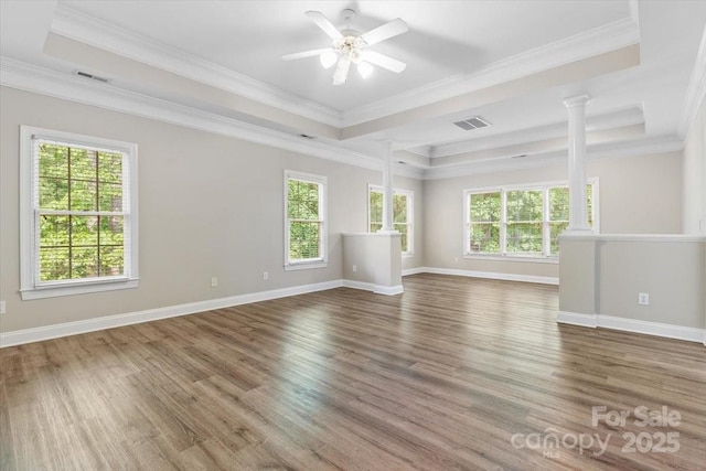 empty room featuring a raised ceiling, wood finished floors, visible vents, and decorative columns