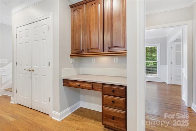 unfurnished office with built in study area, crown molding, and light wood-style floors