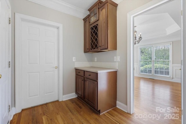 bar with a chandelier, light wood-style flooring, baseboards, and ornamental molding