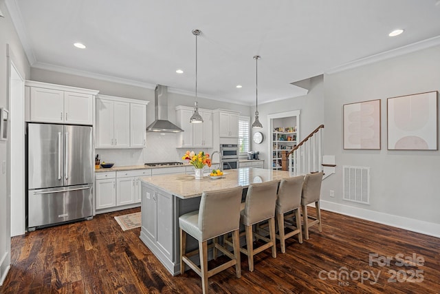 309 Catawba Ave, Davidson, NC 28036 - kitchen featuring appliances with stainless steel finishes, wall chimney range hood, white cabinetry, a breakfast bar area, and a center island with sink