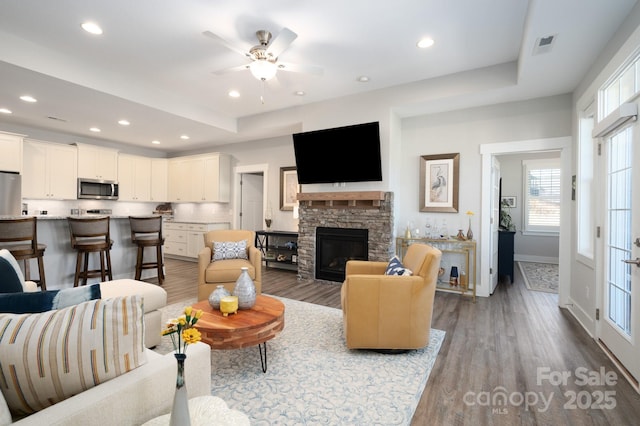 living area with recessed lighting, wood finished floors, a stone fireplace, baseboards, and ceiling fan