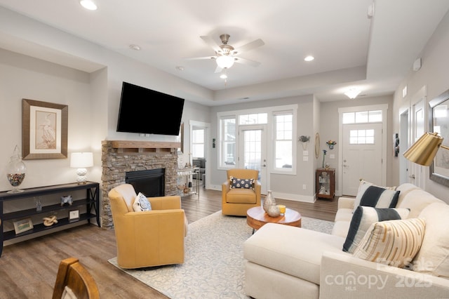 living area featuring a ceiling fan, a stone fireplace, wood finished floors, baseboards, and recessed lighting