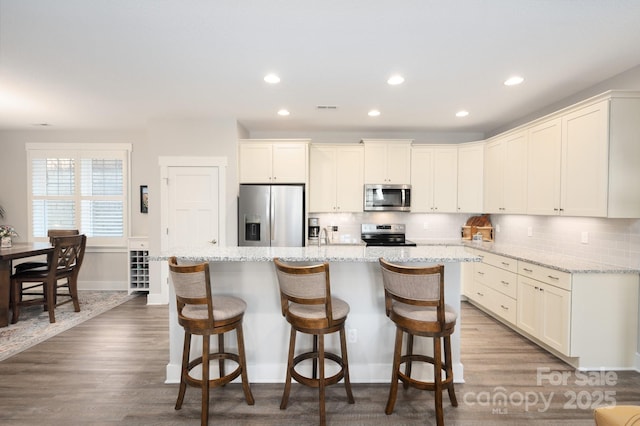 kitchen with wood finished floors, visible vents, a kitchen island, tasteful backsplash, and appliances with stainless steel finishes