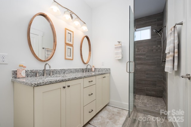 bathroom with baseboards, a sink, double vanity, and a tile shower