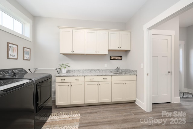 laundry room featuring washing machine and clothes dryer, a sink, light wood-style floors, cabinet space, and baseboards