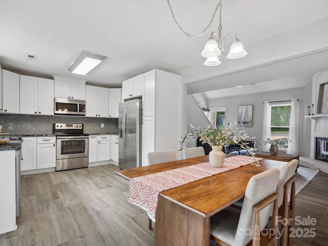 dining space featuring a notable chandelier, a glass covered fireplace, visible vents, and light wood-type flooring
