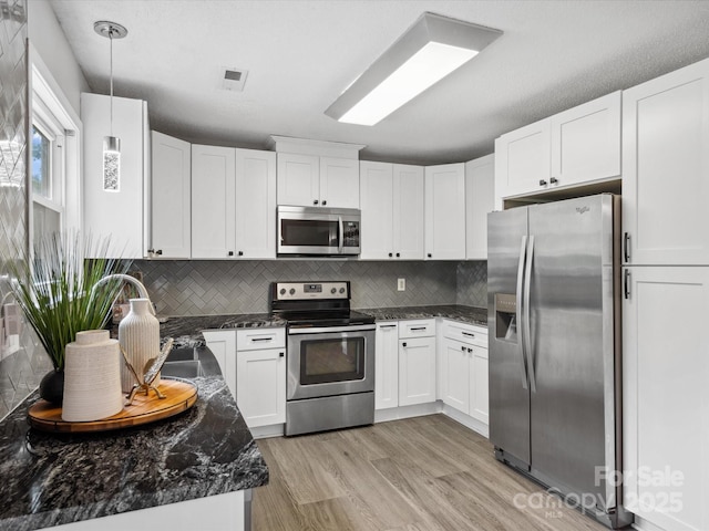 kitchen featuring white cabinets, light wood finished floors, dark stone countertops, stainless steel appliances, and decorative backsplash