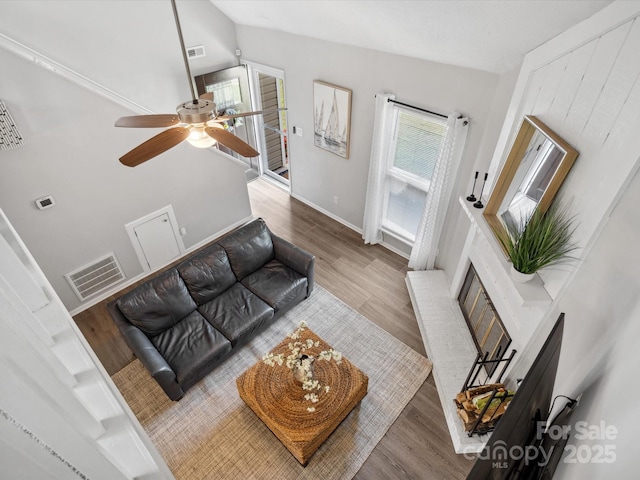 living area featuring visible vents, lofted ceiling, wood finished floors, a fireplace, and ceiling fan
