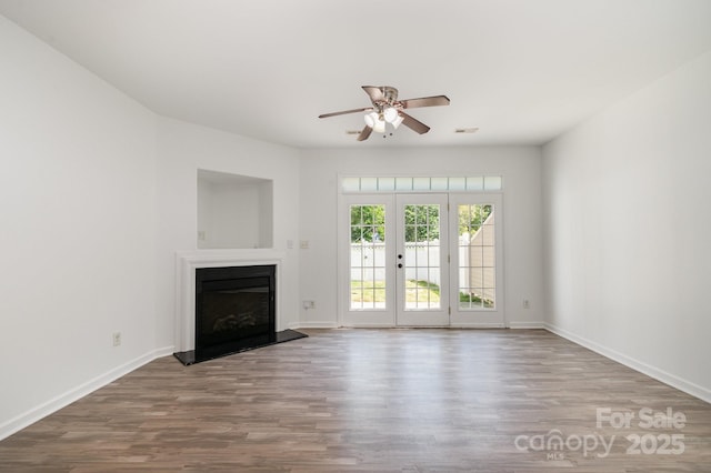 unfurnished living room with baseboards, wood finished floors, a fireplace with raised hearth, and ceiling fan