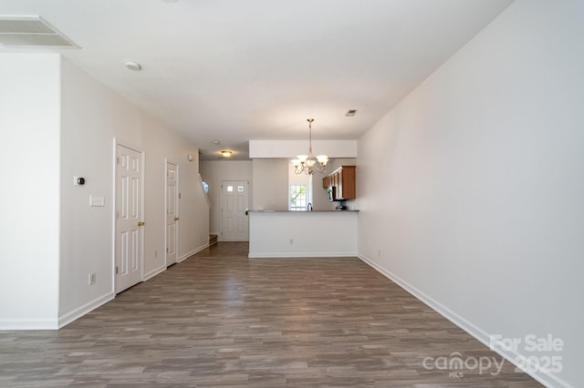 unfurnished living room featuring visible vents, baseboards, wood finished floors, and a notable chandelier