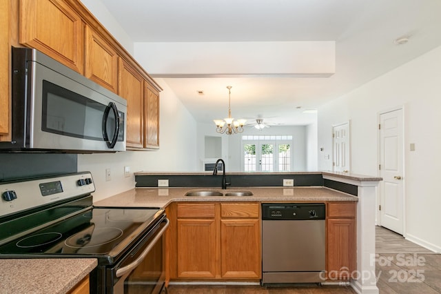 kitchen featuring stainless steel appliances, a peninsula, a sink, a chandelier, and brown cabinetry
