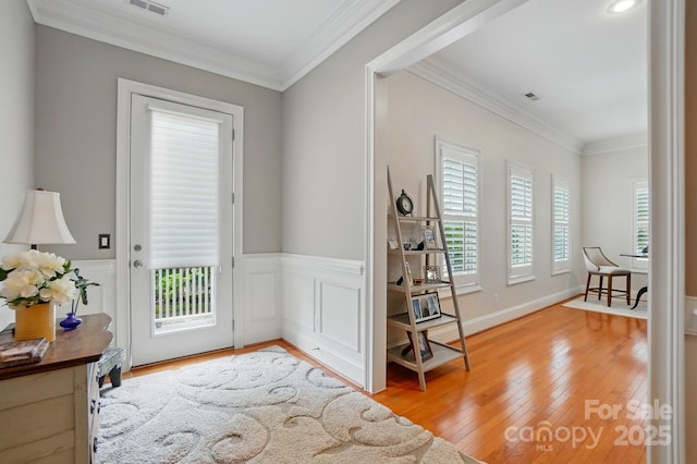 foyer entrance featuring ornamental molding, visible vents, wainscoting, and light wood-style floors