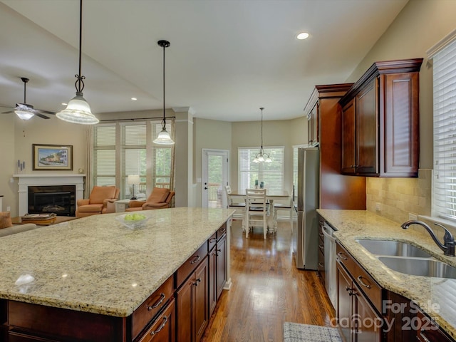 kitchen with dark wood-style flooring, light stone countertops, appliances with stainless steel finishes, a sink, and ceiling fan with notable chandelier