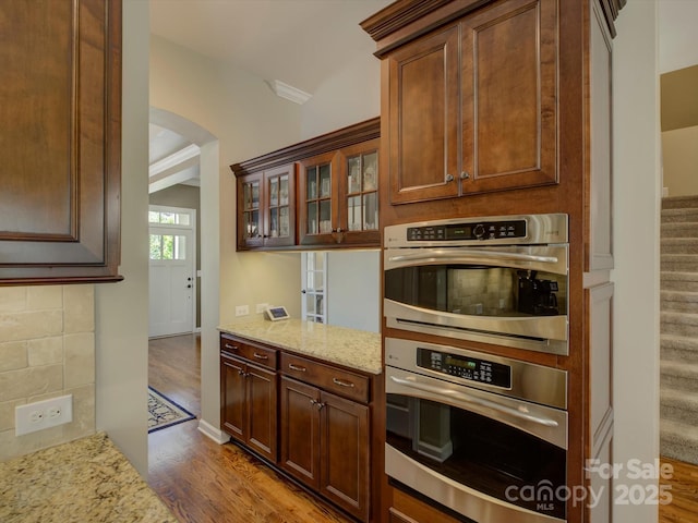 kitchen featuring arched walkways, wood finished floors, light stone countertops, and oven