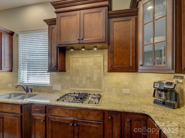 kitchen featuring light stone countertops, glass insert cabinets, tasteful backsplash, a sink, and stainless steel gas stovetop