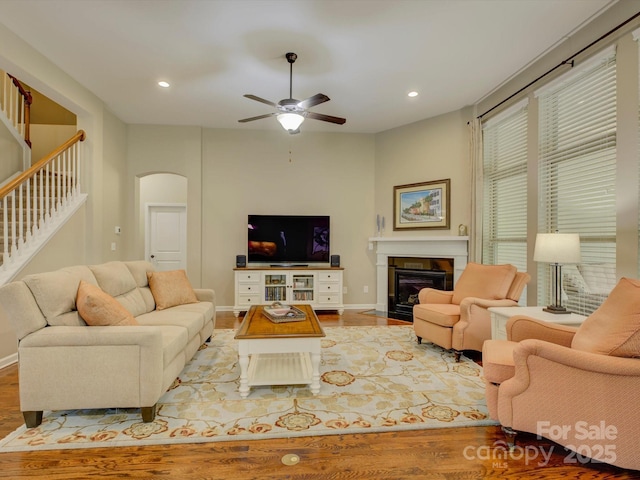 living area with arched walkways, ceiling fan, a fireplace with flush hearth, and wood finished floors