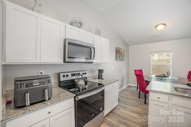 1125 Silvertrace Dr, Salisbury, NC 28144 - kitchen featuring visible vents, appliances with stainless steel finishes, vaulted ceiling, light wood-style floors, and white cabinetry
