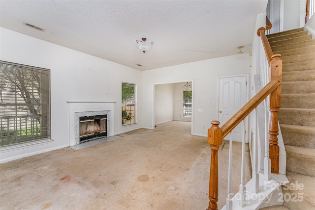 unfurnished living room with a high end fireplace, baseboards, visible vents, and stairs