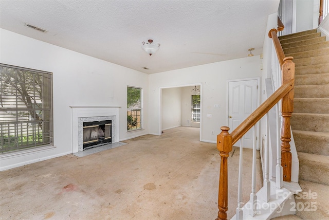 unfurnished living room with a fireplace, baseboards, visible vents, and stairs