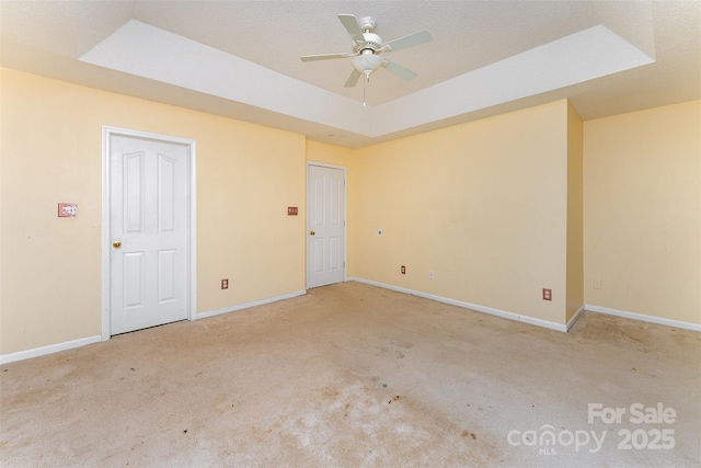 empty room featuring a ceiling fan, baseboards, carpet, and a raised ceiling