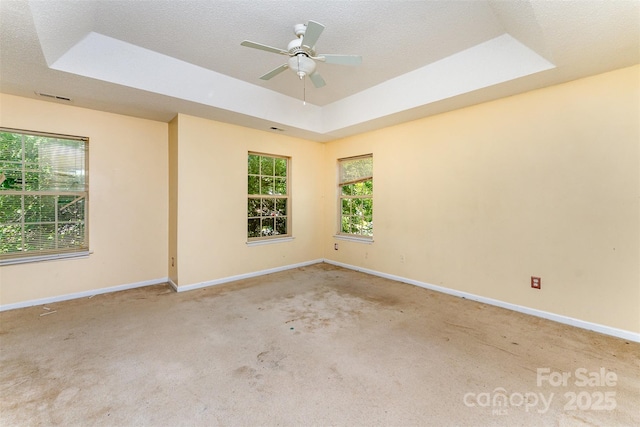 carpeted empty room featuring a tray ceiling, visible vents, baseboards, and ceiling fan
