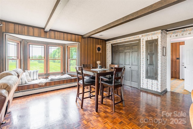 dining room featuring wood walls, a baseboard heating unit, beamed ceiling, baseboards, and a textured ceiling