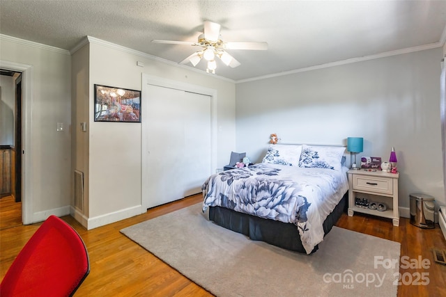 bedroom with crown molding, wood finished floors, a closet, baseboards, and visible vents