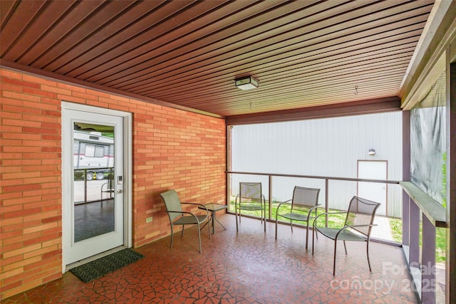 sunroom / solarium featuring wood ceiling and brick wall