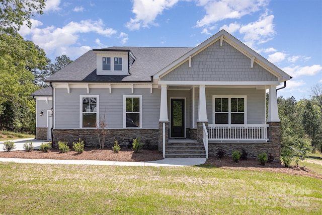 craftsman-style home with a porch, a front lawn, stone siding, and roof with shingles