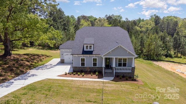 view of front of property featuring a front lawn, driveway, covered porch, stone siding, and roof with shingles