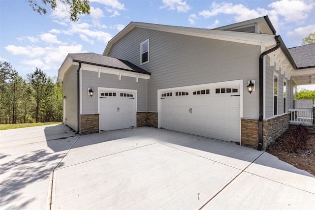 view of home's exterior featuring concrete driveway, stone siding, an attached garage, and roof with shingles